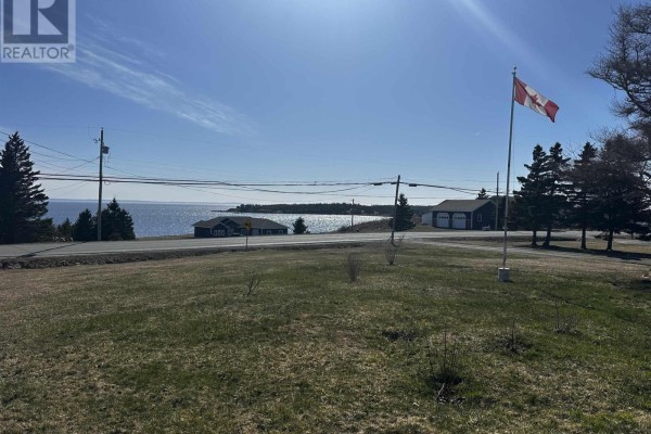View of the ocean and coastline with trees and houses in the distance under a blue sky. - 1659 Ns-206 Highway, West Arichat