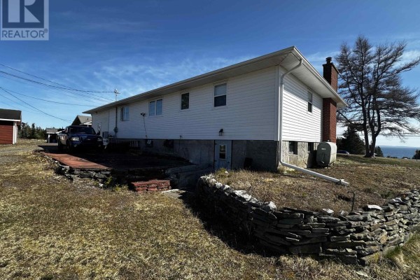 Rear view of the house showing a stone foundation, brick chimney, and grassy yard. - 1659 Ns-206 Highway, West Arichat