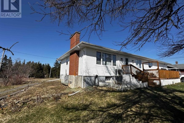 Side view of the house with a brick chimney, white siding, and a wooden deck. - 1659 Ns-206 Highway, West Arichat