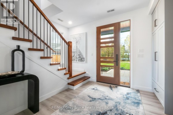 Interior view of a foyer with a wooden staircase, a modern console table, and a glass front door. - 166 Country Side Drive, Chatsworth