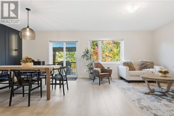 Living and dining area with light wood floors, a white sofa, and a wooden dining table. - 166 Eclipse Crescent, Sudbury