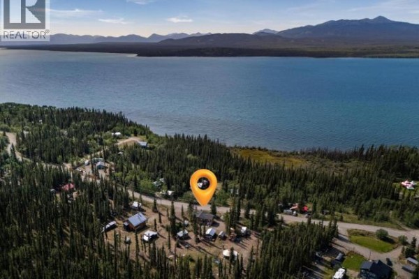 Aerial view of a lakeside community with numerous small structures surrounded by pine forest and a large blue lake. - 166 Judas Creek Drive, Whitehorse South