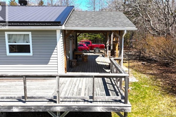 Close-up view of a wooden deck attached to a gray house, with a covered section and red truck visible. - 166 Kerrs Ridge Road, Bocabec