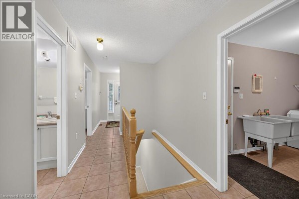 Hallway with tiled floors, a wooden banister leading downstairs, and doors to rooms. - 166 Toby Crescent, Hamilton