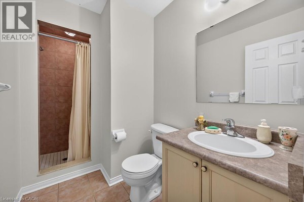 Bathroom with a toilet, vanity with sink, and a shower stall with a tan curtain. - 166 Toby Crescent, Hamilton