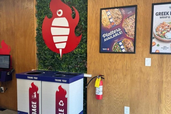 Close up of a green wall with a red shawarma logo, recycling bins, and a fire extinguisher. - 1660 Queen Street W, Toronto