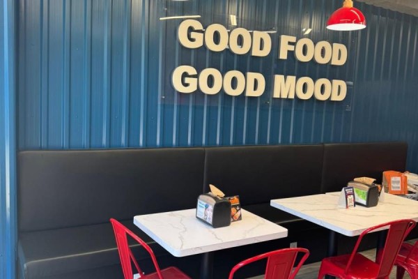 Restaurant seating area with black banquettes, white tables, red chairs, and a blue corrugated metal wall. - 1660 Queen Street W, Toronto