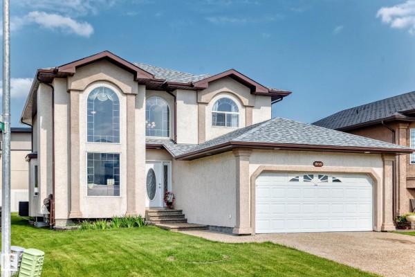 Side exterior view of a two-story beige house with a white garage door and arched windows. - 16619 72 St Nw, Edmonton