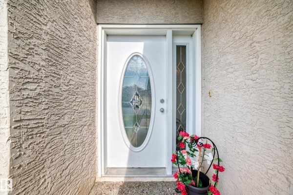 Close-up of the white front door with an oval leaded glass window and textured siding. - 16619 72 St Nw, Edmonton