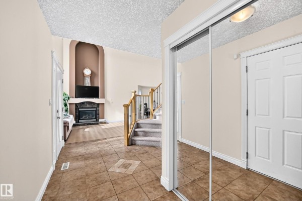 Interior view of the beige entryway with a fireplace, stairs, tiled floors, and mirrored closet doors. - 16619 72 St Nw, Edmonton
