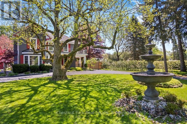 A tiered stone fountain sits on a lawn in front of a grey house and tree. - 1663 5th Avenue E, Owen Sound