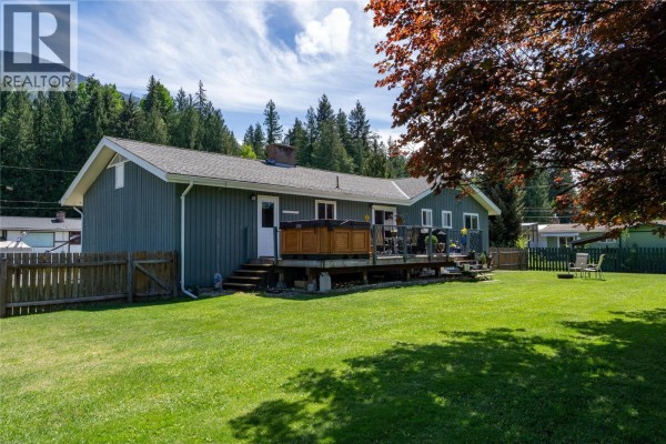 The grey house is situated on a street with snow-dusted mountains in the background. - 1669 Hiob Road, Revelstoke