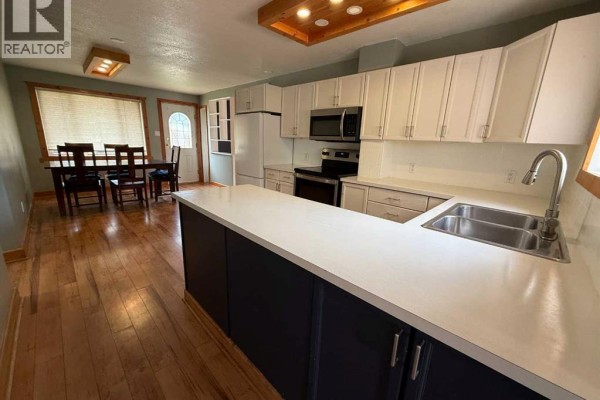 Dining area with a wood dining table, chairs, and blue curtains beside a window. - 167 Sunwapta Drive, Hinton