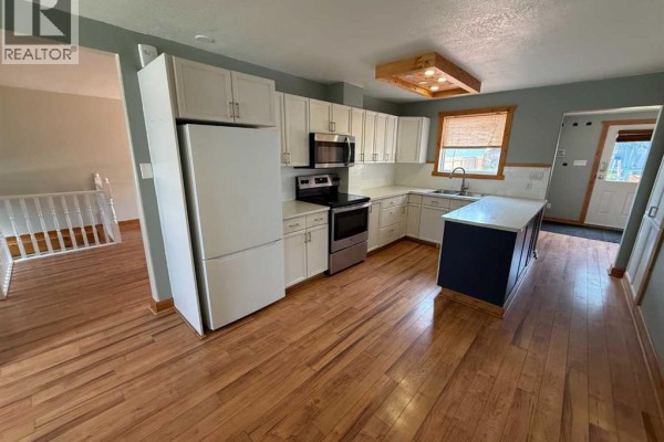 Kitchen with white cabinets, stainless steel appliances, and a navy blue island with a white countertop. - 167 Sunwapta Drive, Hinton