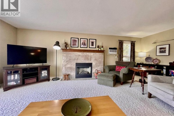 Living room with a fireplace, sofa, chairs, coffee table, and view into dining area. - 1672 Thayer Court, Kelowna