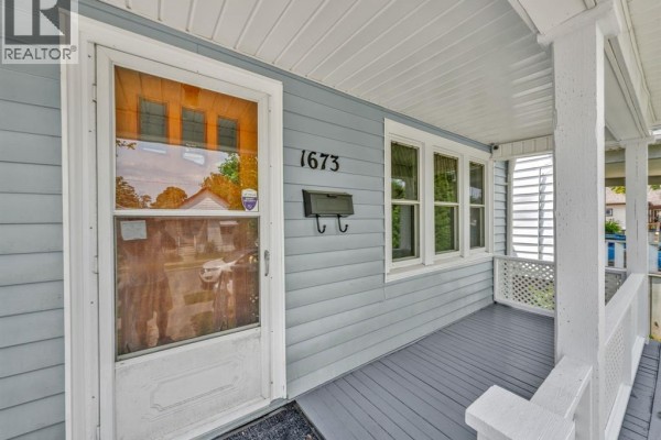 Close-up of the front door and porch with light blue siding, white trim, and windows. - 1673 Cadillac Street, Windsor