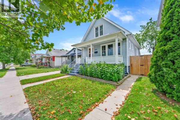 Side view of a light blue house on a street with green lawns and trees. - 1673 Cadillac Street, Windsor