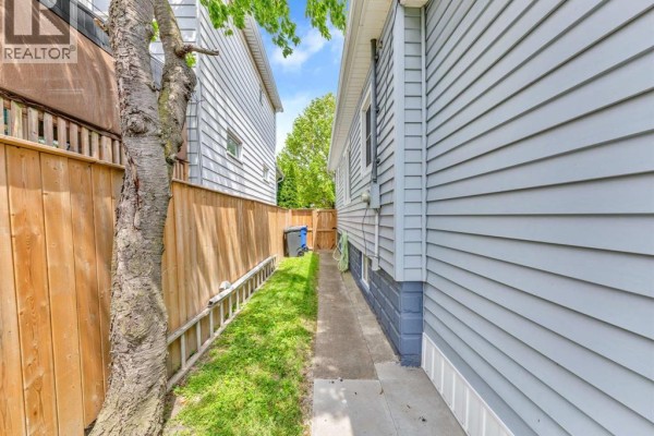 Narrow grassy side yard between a wooden fence and the light blue siding of a house. - 1673 Cadillac Street, Windsor