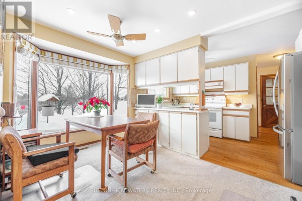 Kitchen with white cabinets, a dining table near a bay window overlooking a snowy landscape. - 16735 Mississauga Road, Caledon