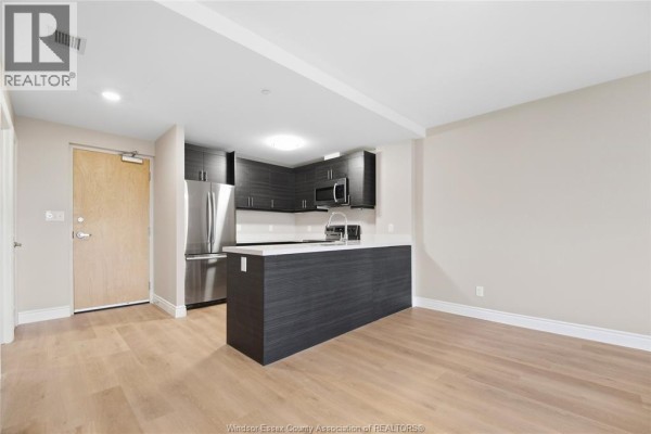Open concept living area and kitchen with light wood floors, dark cabinets, and stainless steel appliances. - 1675 Banwell Road Unit# 404, Windsor