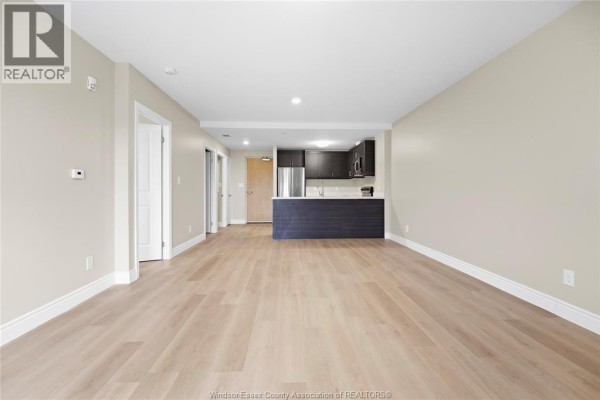View of living room and kitchen area with light wood floors and neutral wall color. - 1675 Banwell Road Unit# 404, Windsor