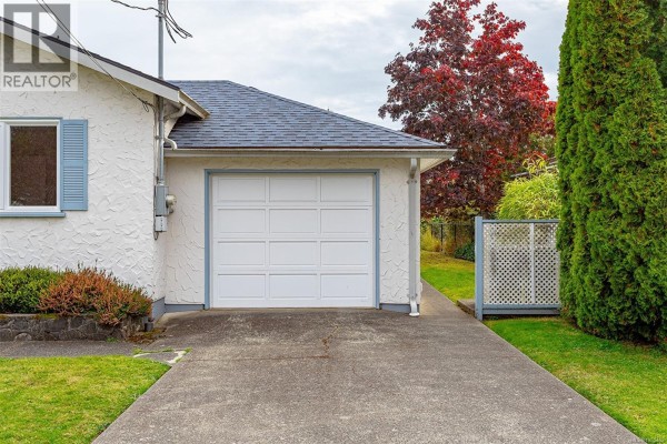 Concrete driveway leading to a white, panelled garage door on the side of a white stucco house. - 1679 Freeman Ave, Saanich