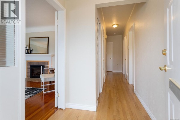 Interior view of a long, bright hallway with light wood floors and white doors. - 1679 Freeman Ave, Saanich