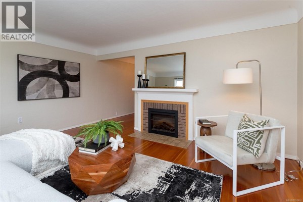 Living room with hardwood floors, a white fireplace, modern furniture, and abstract wall art. - 1679 Freeman Ave, Saanich