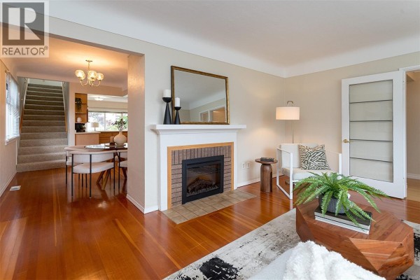View of the living room, fireplace, and dining area with a staircase visible to the left. - 1679 Freeman Ave, Saanich
