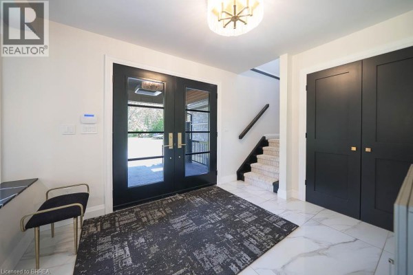 Entrance foyer with double glass doors, black stairs, and dark gray closets. - 1679 Highway 6, Port Dover