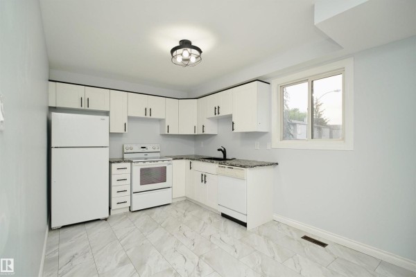 L-shaped kitchen with white cabinets, granite countertops, and a window overlooking the exterior. - 1679 Lakewood Rd S Nw, Edmonton
