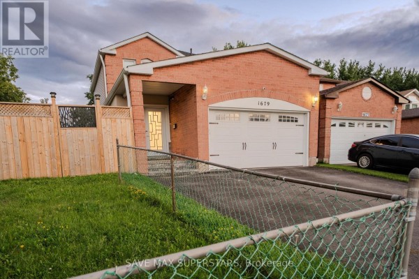 A view of the house from the side shows a red brick exterior, a garage, and a grassy lawn. - 1679 Portland Court, Pickering