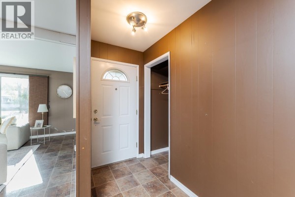 Foyer with a white front door, dark brown wood paneling, and a closet. - 168 Aitken Crescent, Prince George
