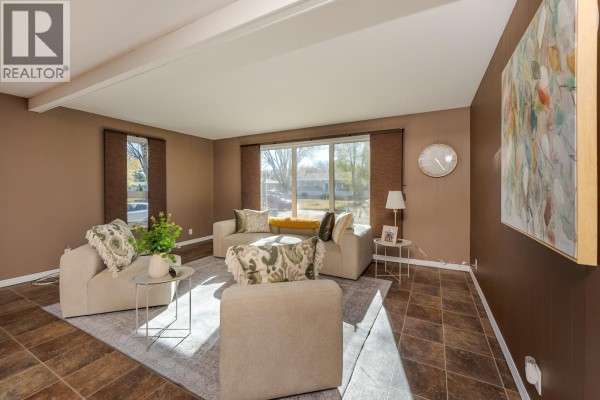 Living room with beige furniture, a large picture window, and dark brown paneled walls. - 168 Aitken Crescent, Prince George