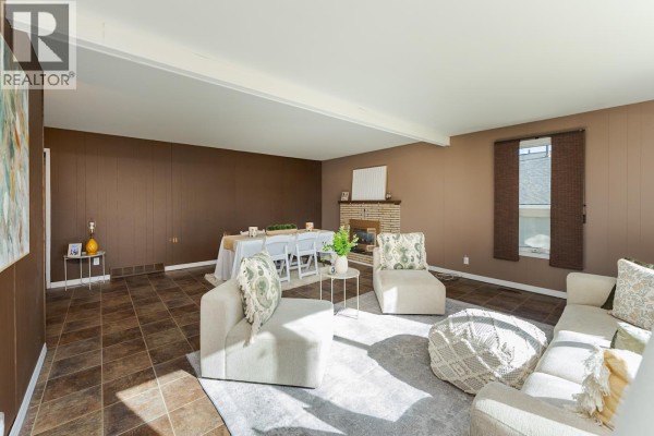 Living and dining area with a fireplace, dining table, and beige sectional seating. - 168 Aitken Crescent, Prince George