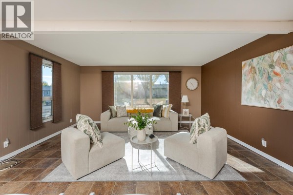 Living room with a large window, beige sofas, chairs, and abstract wall art. - 168 Aitken Crescent, Prince George