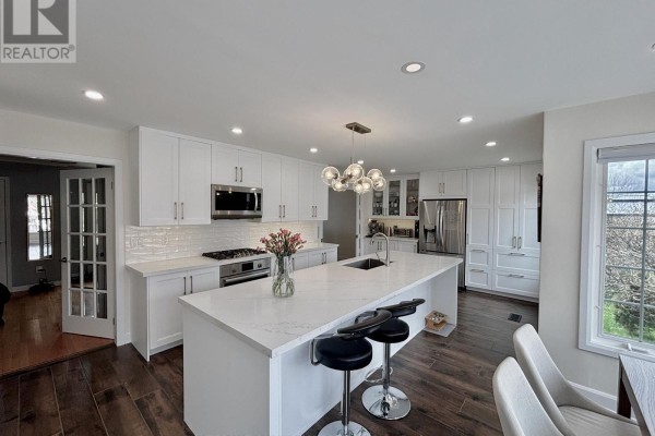Modern white kitchen with island, stainless steel appliances, and hardwood floors. - 168 Willow Lane, Newmarket