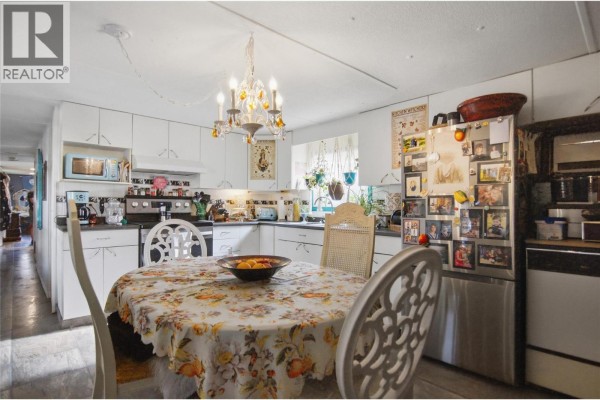 Kitchen with white cabinets, stainless steel appliances, and a floral-covered dining table. - 1680 Lac Le Jeune Road Unit# 22, Kamloops
