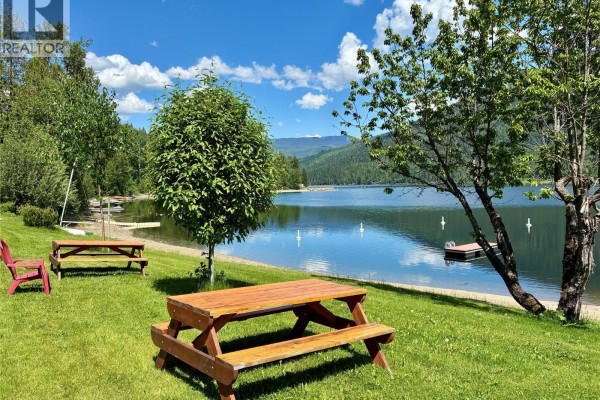Lush green lawn with picnic tables and signage near a tranquil lake. - 1681 Sugar Lake Road Unit# 49, Cherryville