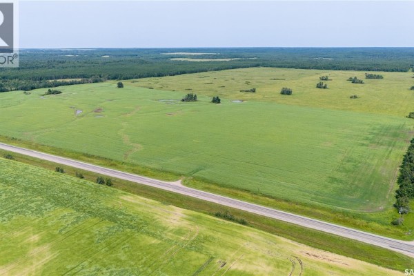 Aerial view of a vast green agricultural field bordered by a highway and a dense treeline. - 1685 Acres Mixed Use Land Near Spiritwood, Medstead Rm No 497