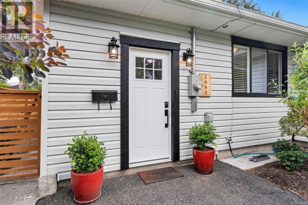 Close-up view of the white front door with a glass pane and black trim, flanked by planters. - 1685 Midgard Ave, Saanich