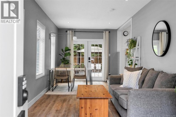 Living and dining area with a grey sofa, wooden coffee table, and chairs near glass doors. - 1685 Midgard Ave, Saanich