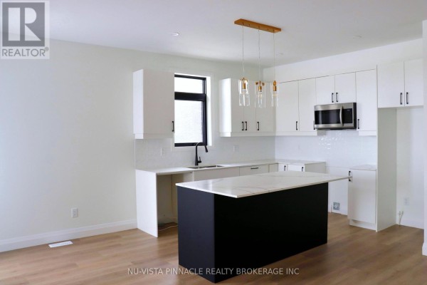 Bright kitchen and dining area with white cabinetry, stainless steel appliances, and a dark island. - 169 - 3900 Savoy Street, London South