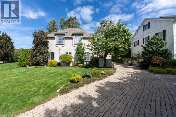 Front view of the light grey two-story house with a curved brick driveway and manicured lawn. - 169 John Street W, Niagara On The Lake