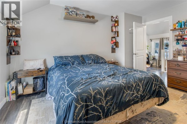 Bedroom with queen bed, blue floral bedding, nightstand, and shelving - 169 Lorne Avenue Chatham
