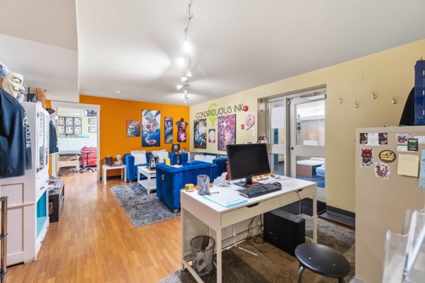 Reception area with desk, computer, blue sofas, and orange accent wall. - 169 Marion St, Winnipeg