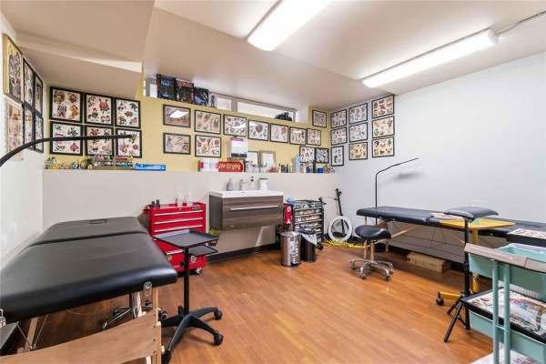 Tattoo studio workspace featuring multiple tattoo beds, a sink, storage carts, and artwork. - 169 Marion Street, Winnipeg