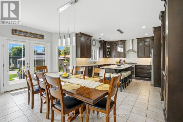 Open concept kitchen and dining area with dark wood cabinets, granite countertops, and a large wooden dining table. - 169 Michael Drive, Welland