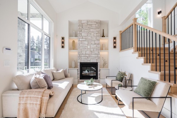 Living room with a vaulted ceiling, large windows, a stone fireplace, and light-colored furniture. - 16908 1 Avenue, Surrey