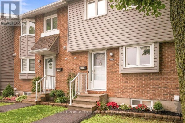 Close-up of red brick townhouse exterior with grey siding, white doors, and manicured landscaping. - 1699e Lamoureux Drive, Ottawa